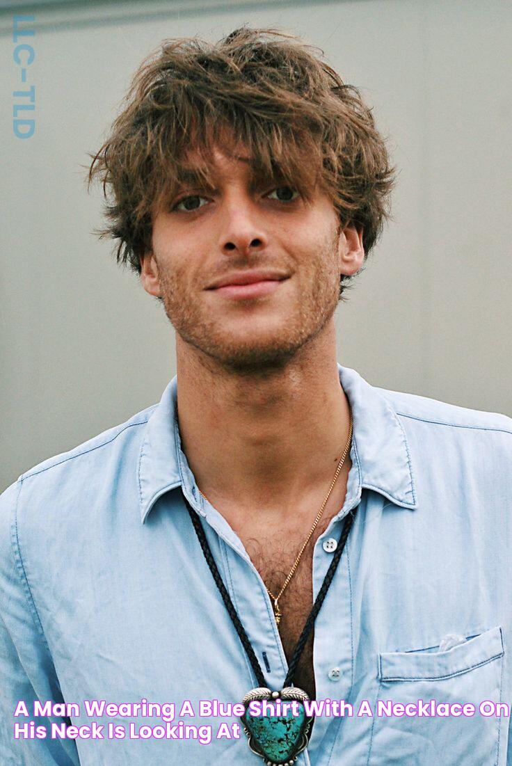 a man wearing a blue shirt with a necklace on his neck is looking at