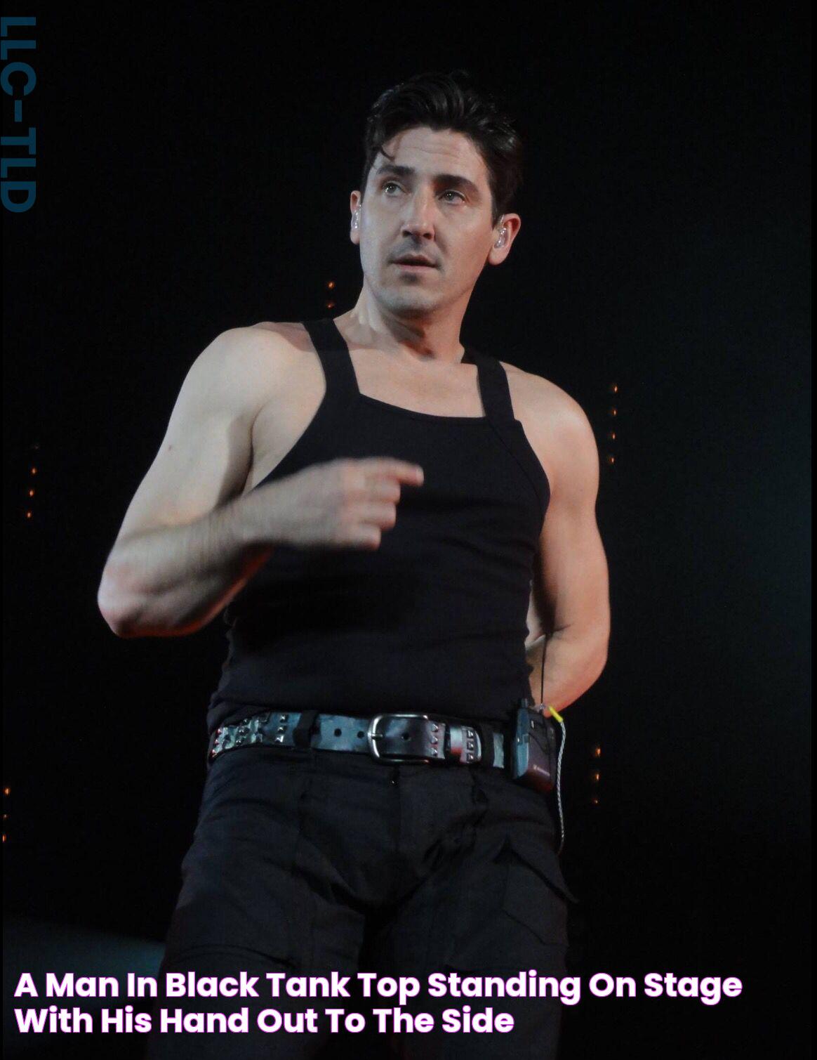 a man in black tank top standing on stage with his hand out to the side